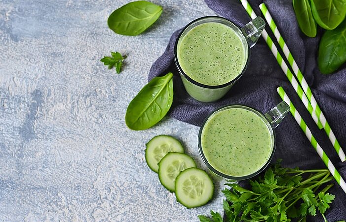 Grüner Abnehmshake mit Gurke, Spinat und grünen Strohhalmen in zwei Gläsern