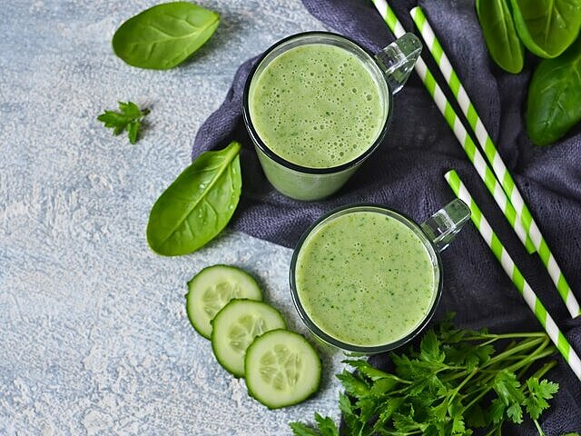 Grüner Abnehmshake mit Gurke, Spinat und grünen Strohhalmen in zwei Gläsern